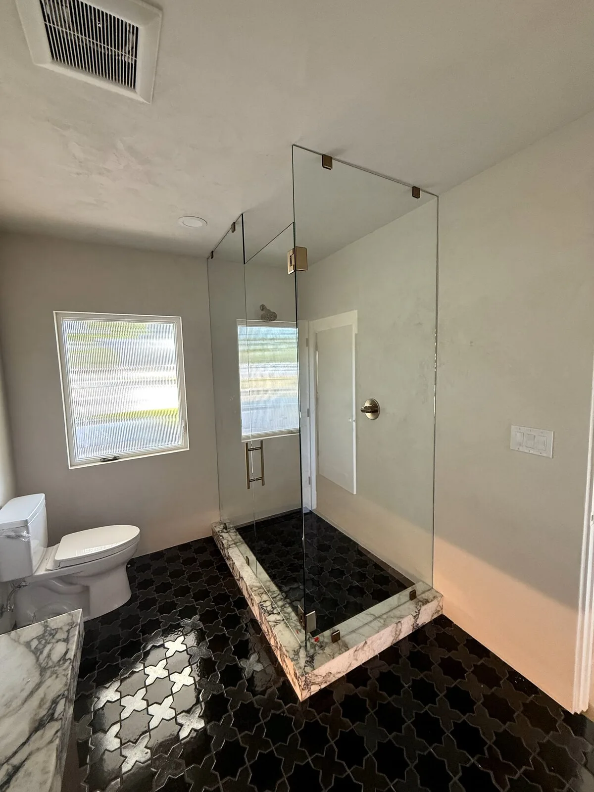 Frameless glass shower panel over black patterned tile with a marble curb