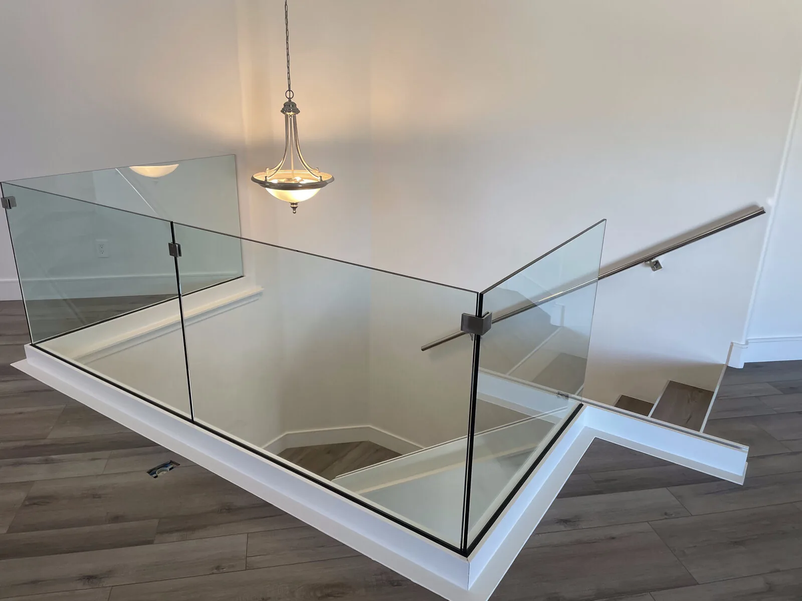 Frameless glass railing with clamp mounts around a second-story landing and staircase in a Fresno home