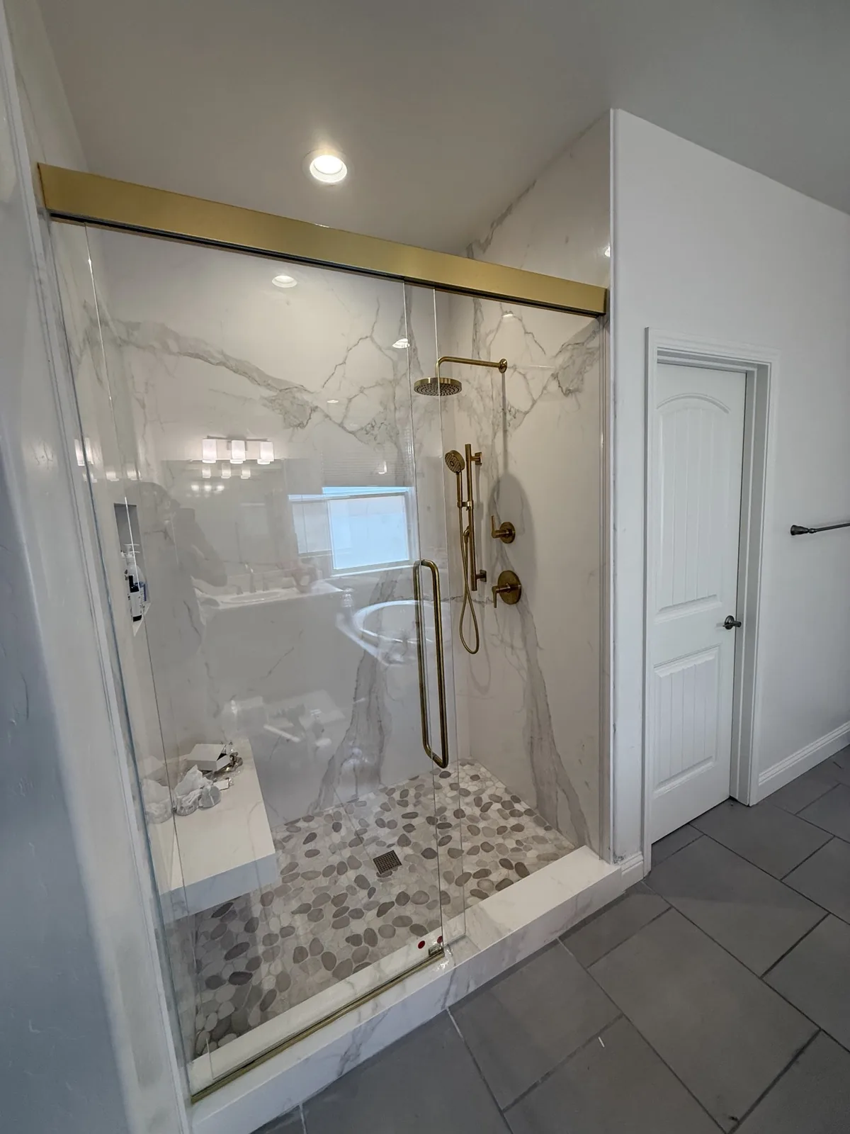 Frameless sliding shower door with brushed gold header and hardware over white marble tile