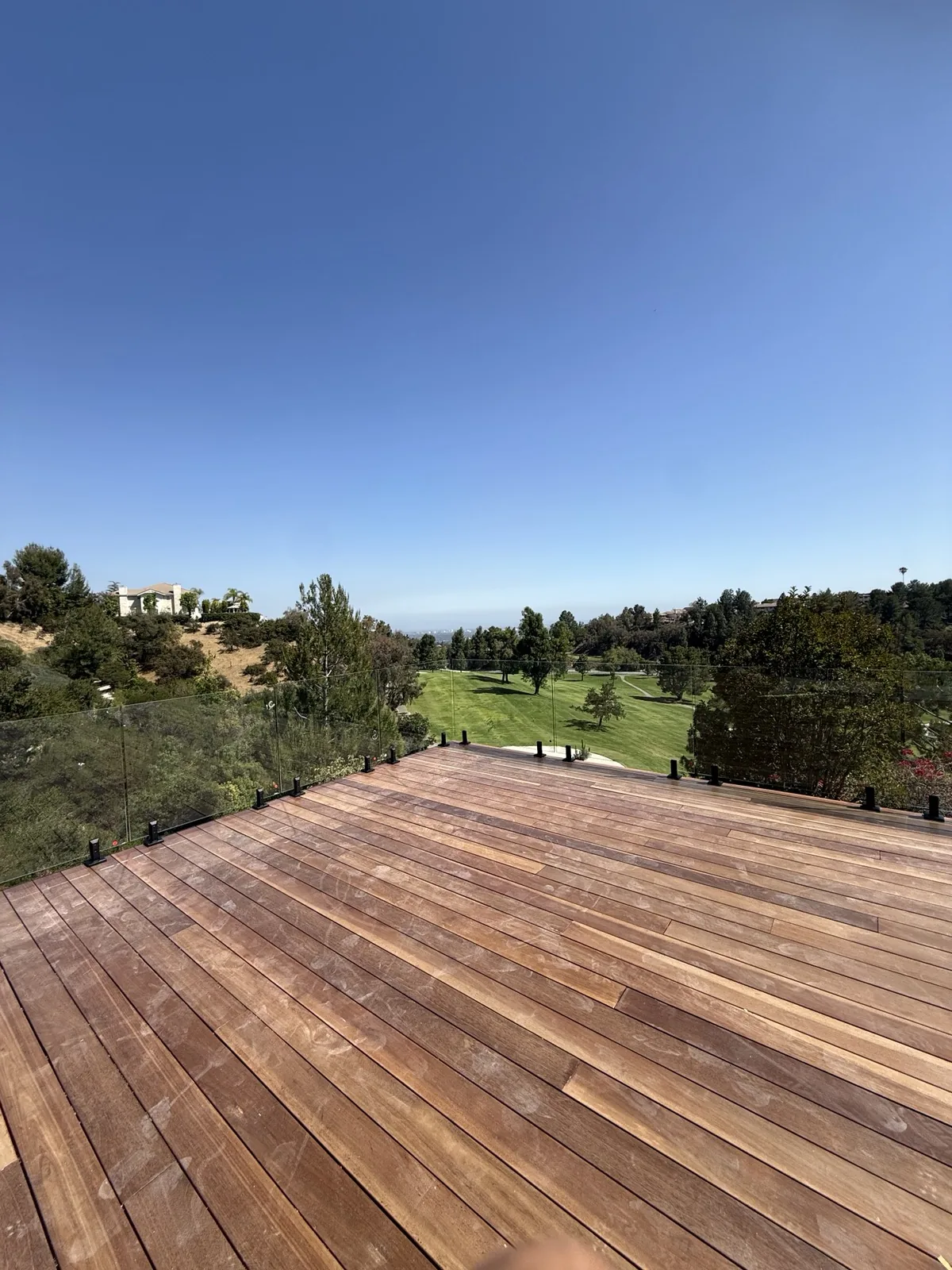 Frameless glass railing on standoffs along the edge of a hillside wood deck overlooking a golf course