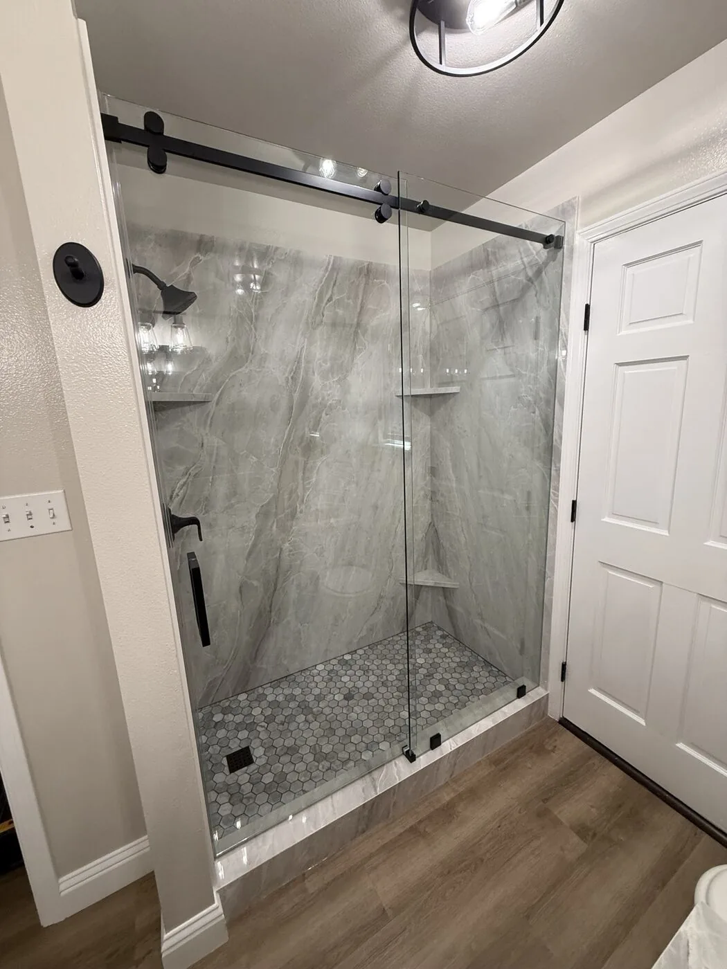 Frameless sliding shower door with matte black hardware over marble-look tile, installed by California Glass Railing